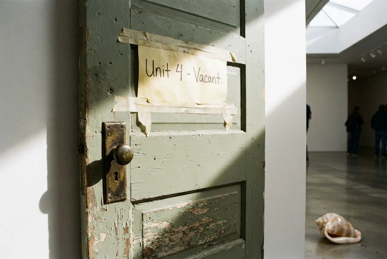 A tight, eye-level detail shot of a weathered, sage-green wooden door salvaged from a North 19th Avenue cottage, now mounted on a white gallery wall at Interim
