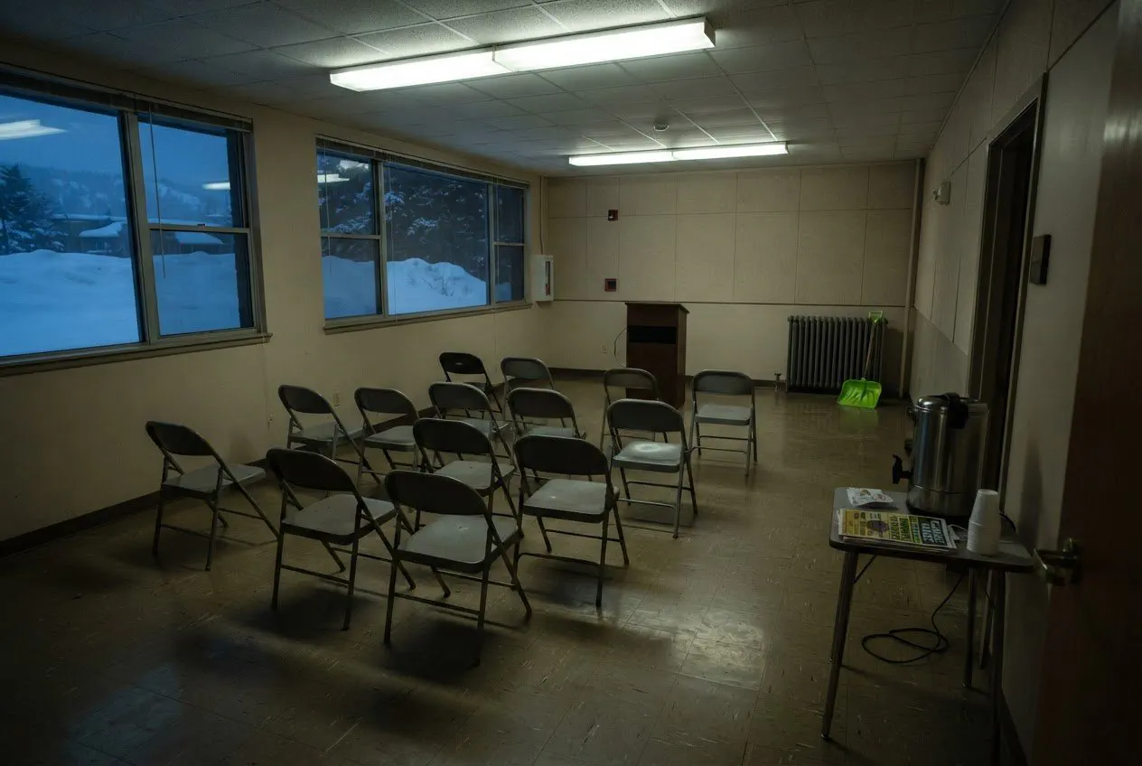 A wide-angle, eye-level shot of the basement meeting room in the Bozeman Public Library, captured in the dim, flickering hum of late-afternoon fluorescent